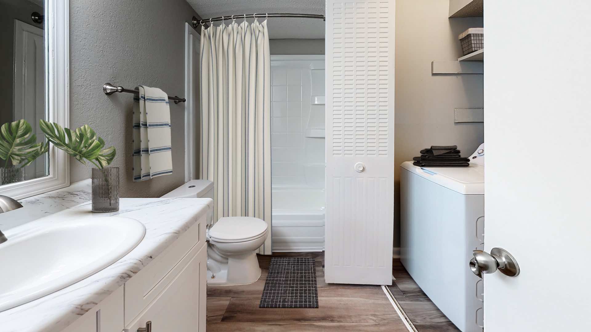 bathroom with convenient curved shower rod and washer/dryer unit in laundry closet